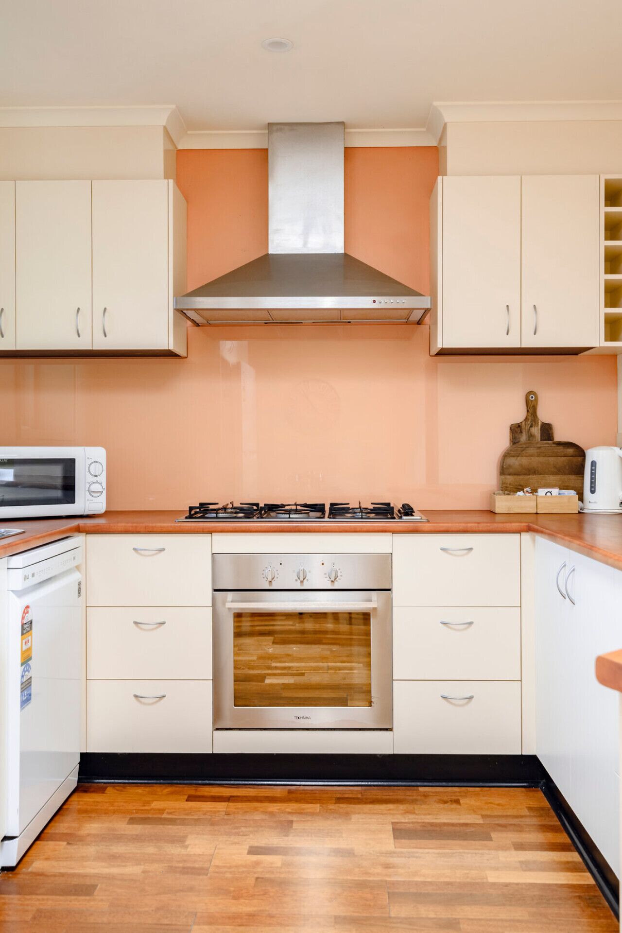 Una cocina con gabinetes blancos, una campana extractora de acero inoxidable, un microondas, una estufa y un horno empotrado.