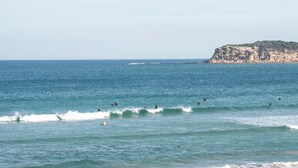 Une plage avec des vagues, une rive sablonneuse et une falaise qui se dessine à l’horizon.