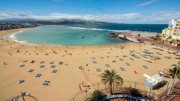 Uma praia com espreguiçadeiras e guarda-sóis, um cais e um edifício com uma placa.