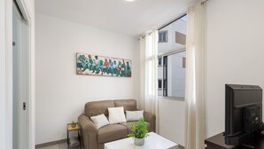 Uma sala de estar com um sofá, uma mesa de centro com uma planta, uma televisão e um quadro na parede.