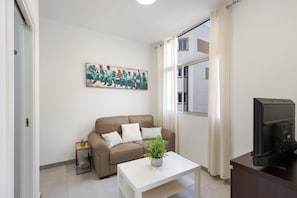 Ein Wohnzimmer mit einer Couch, einem Couchtisch mit Pflanze, einem Fernseher und einem Bild an der Wand.