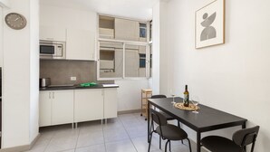 Cozinha compacta com armários brancos, micro-ondas e área de refeições com mesa e cadeiras.