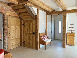 A rustic interior with exposed wooden beams, a wooden bench with a red and white cushion, and a brick wall.