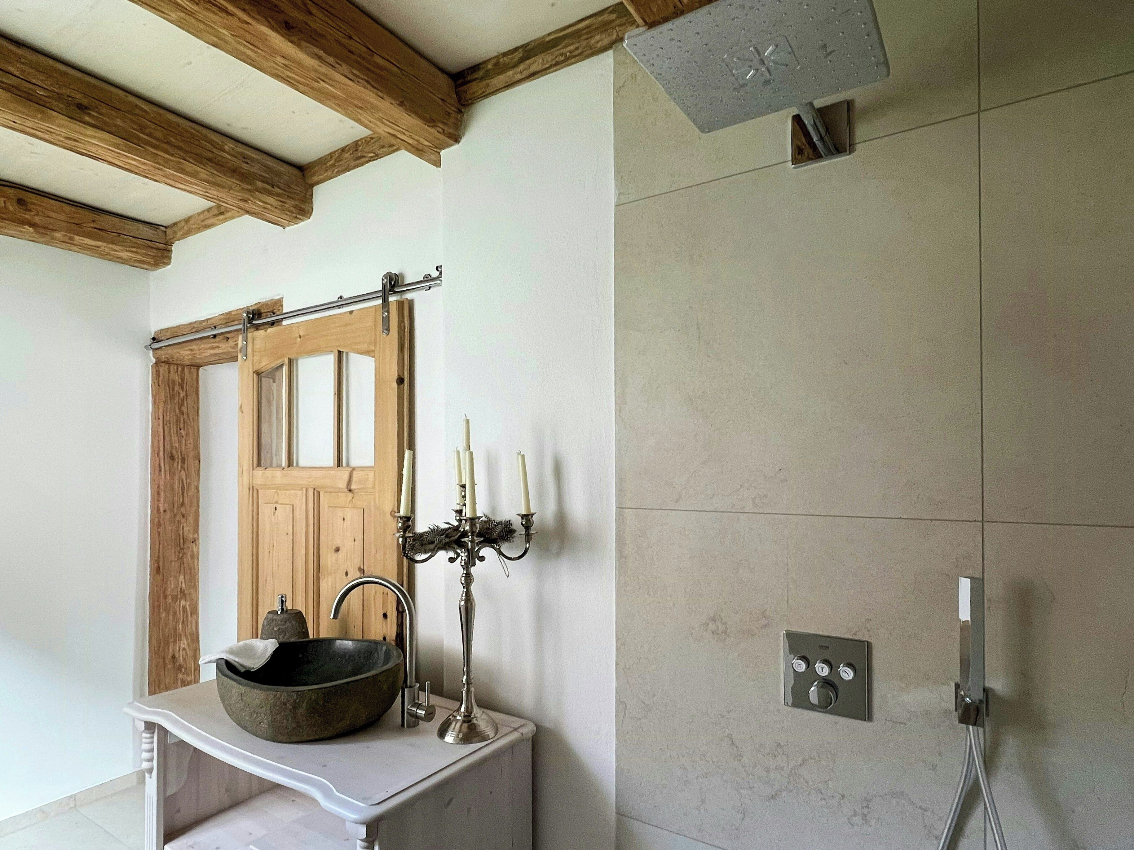 Un baño con puerta de madera, un lavabo de piedra, un candelabro y una ducha con panel de control.