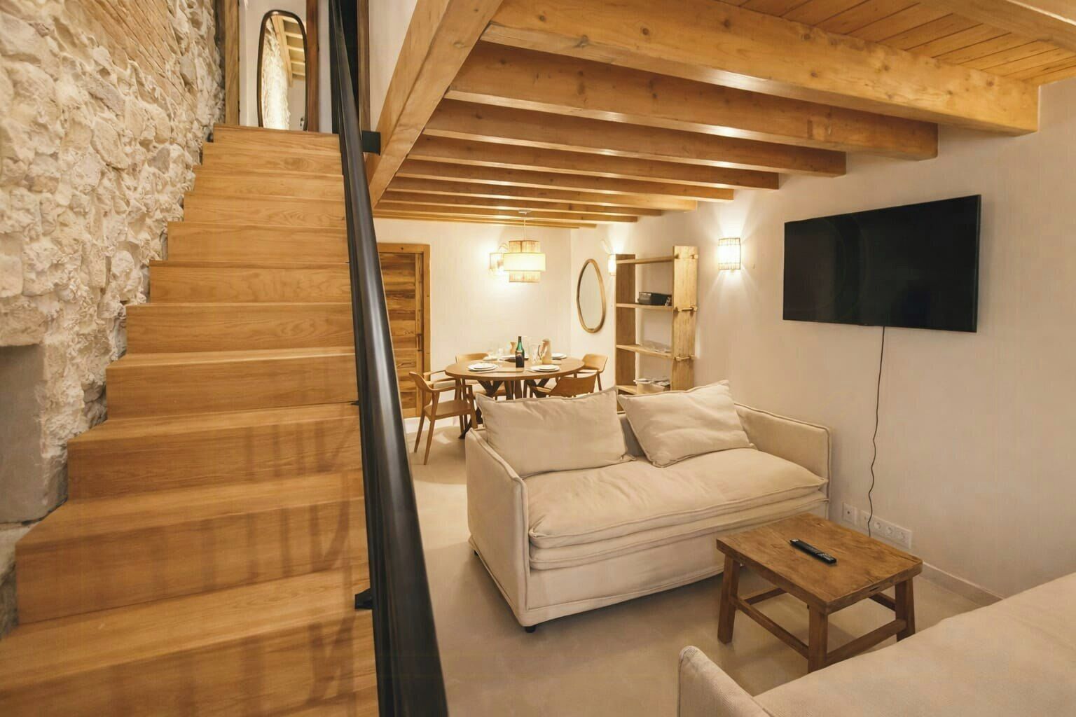 Una escalera conduce a una sala de estar con un sofá, una mesa y un televisor montado en la pared.