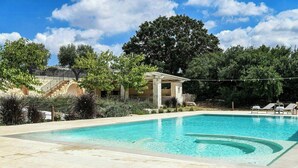 En swimmingpool med et pergolaområde, liggestole og en stentrappe, der fører op til en bygning.