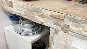 A kitchen with a stone backsplash, a bread loaf, and a trash bin.