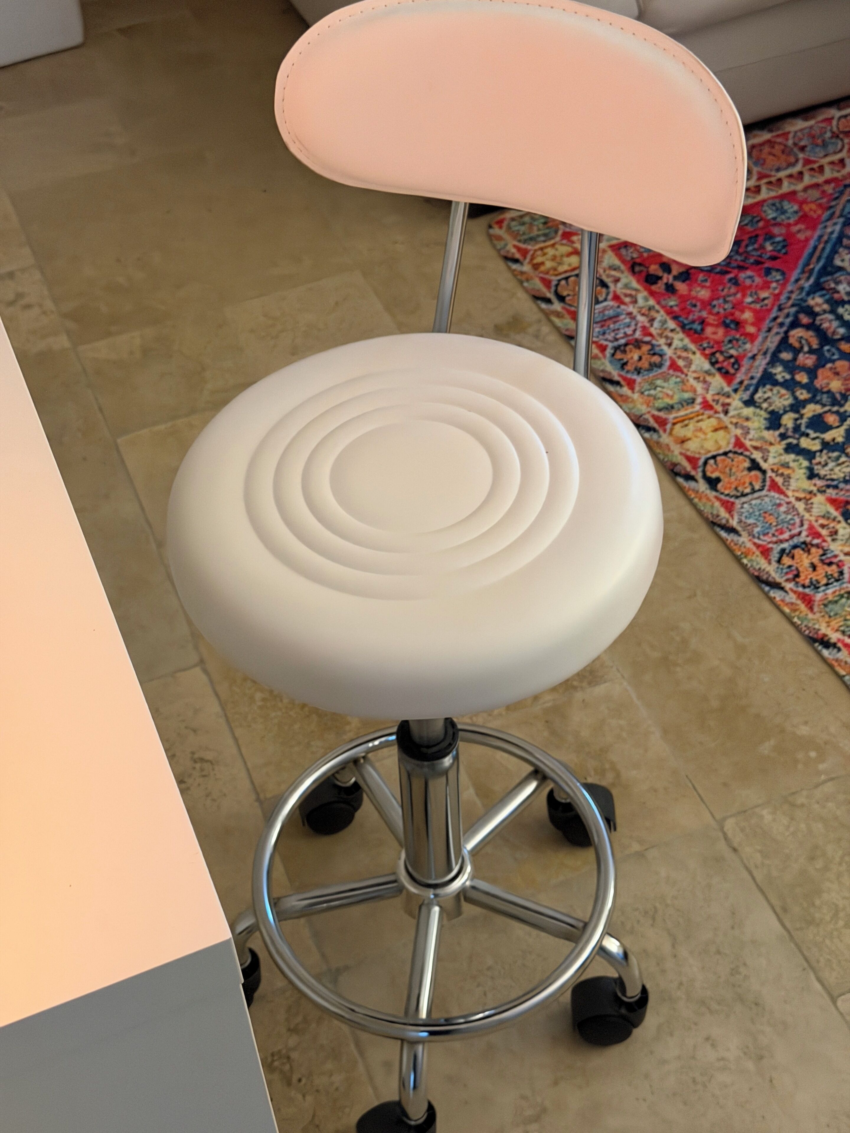 Une chaise de bureau blanche, dotée d’un haut dossier et d’un piédestal en métal muni de roulettes.
