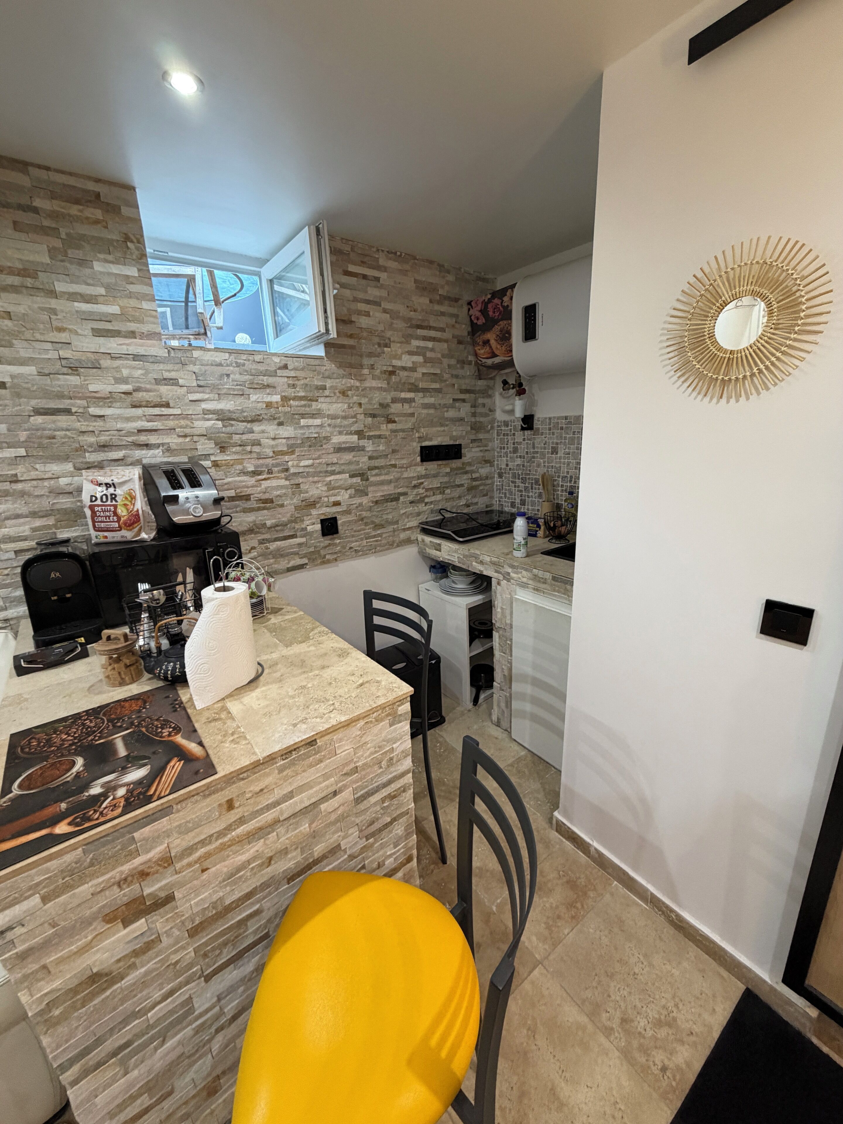 Una cocina con salpicadero de piedra, un tostador, un hervidor y una silla amarilla.