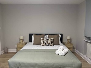 A bedroom with a bed, two bedside tables with lamps, a radiator, and a wall-mounted TV. - Huge Modern 3 Bed Flat Central For Sightseeing (London)