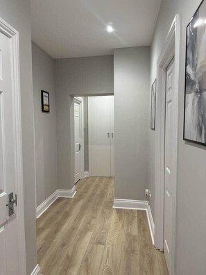 A hallway with wooden flooring, white walls, and doors leading to other rooms. - Huge Modern 3 Bed Flat Central For Sightseeing (London)
