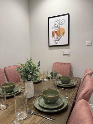 A dining table set with green plates and bowls, pink chairs, and a framed artwork on the wall. - Huge Modern 3 Bed Flat Central For Sightseeing (London)