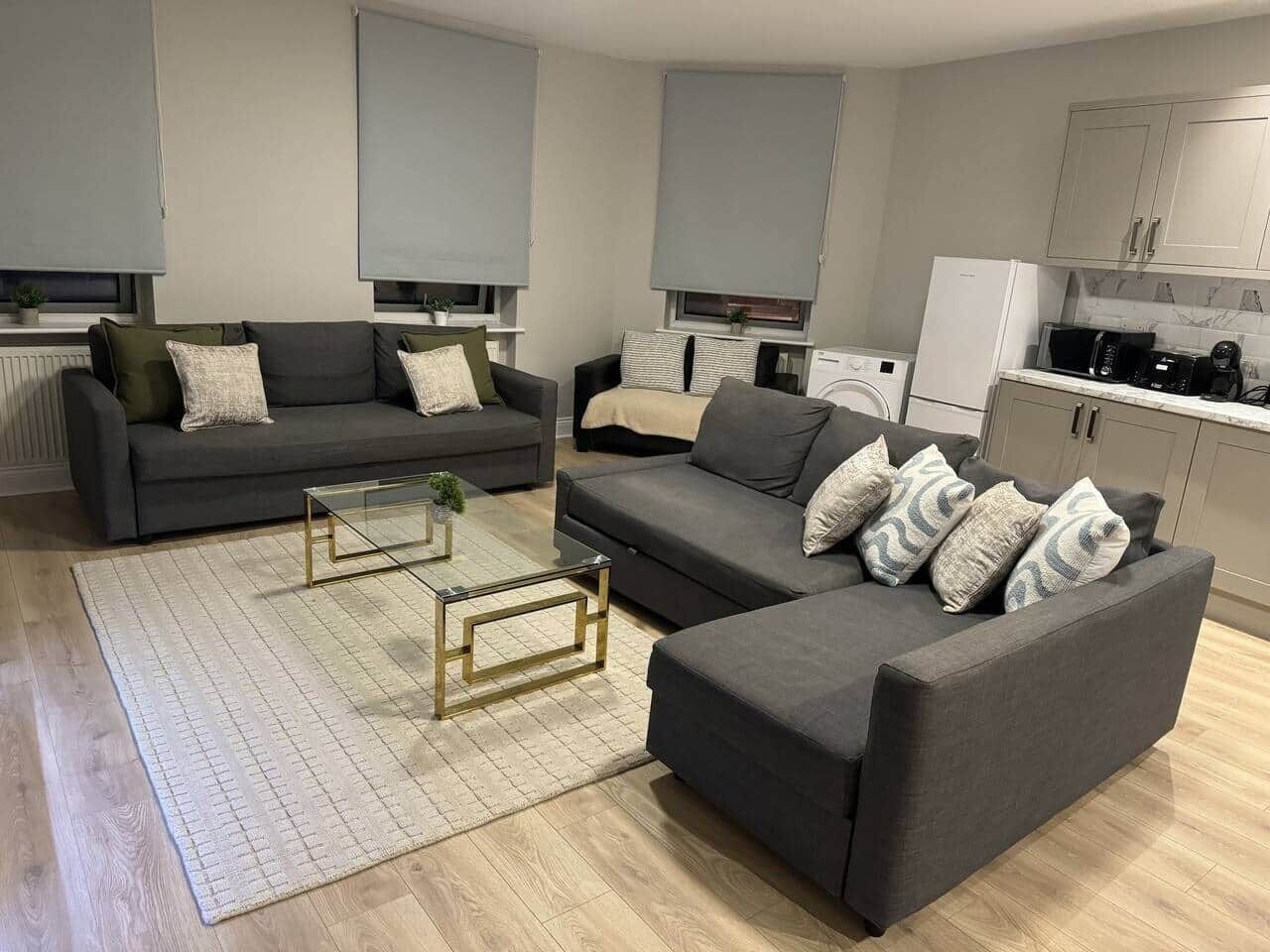 Een woonkamer met twee banken, een salontafel en een keuken met kasten en apparatuur.