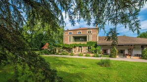 Une maison à deux étages dotée d’un balcon, entourée de verdure et d’une pelouse bien entretenue.
