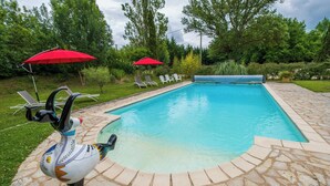 Une piscine bordée de pierres, avec des chaises longues et des parasols rouges.