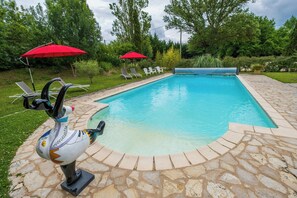 Ein Swimmingpool mit Steinbord, Liegestühlen und roten Sonnenschirmen.