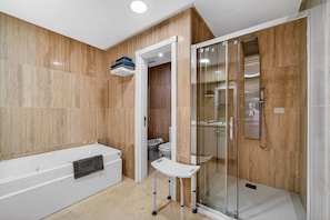 Een moderne badkamer met een bad, een douchecabine en een klein wit krukje.