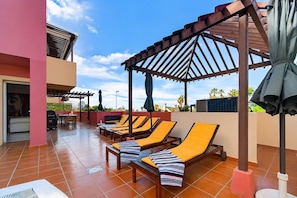 Een dakterras met ligbedden, een pergola en uitzicht op palmbomen.