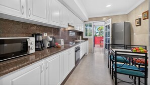 Una cocina con armarios blancos, microondas, cafetera y refrigerador.