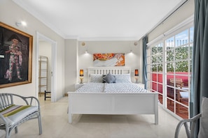 Een slaapkamer met een bed, een stoel, een schilderij en een raam met uitzicht.