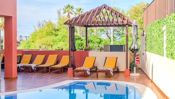 Zona de piscina con sillones de descanso, una pérgola y vistas al verdor.