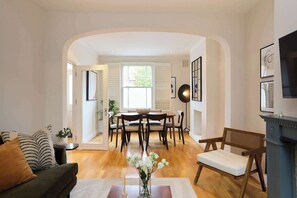 Ein Wohnzimmer mit einer Couch, einem Esstisch mit Stühlen, einem Kamin und einem großen Fenster.