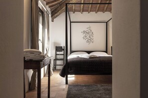 Ein Schlafzimmer mit einem Himmelbett, einem Nachttisch mit Handtüchern, einem Sessel und einem an der Wand befestigten Kunstwerk.