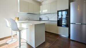 Una cocina moderna con armarios blancos, un refrigerador de acero inoxidable y una isla central con taburetes de bar.