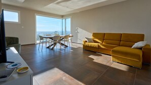Una sala de estar moderna con un sofá, una mesa de comedor con sillas, un televisor y un ventanal con vistas.