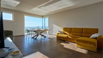 Un salon moderne comprenant un canapé, une table à manger avec des chaises, un téléviseur et une grande fenêtre donnant sur un beau paysage.