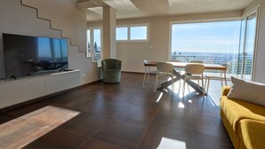 Una sala de estar moderna con una televisión de pantalla plana, una escalera, un área de comedor con sillas y un sofá amarillo.