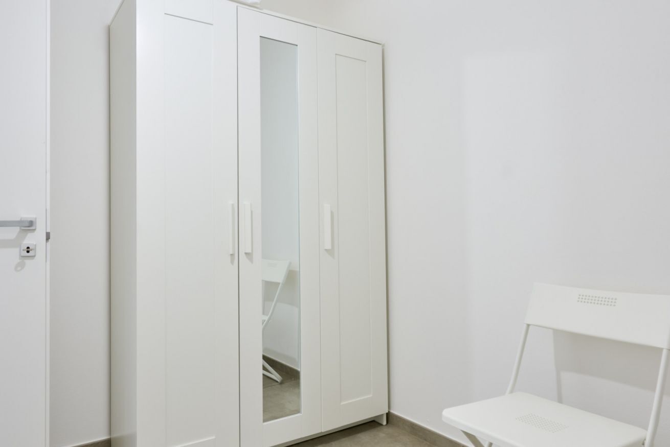 Ein weißer Kleiderschrank mit Spiegelüren, ein weißer Stuhl und eine weiße Wand.