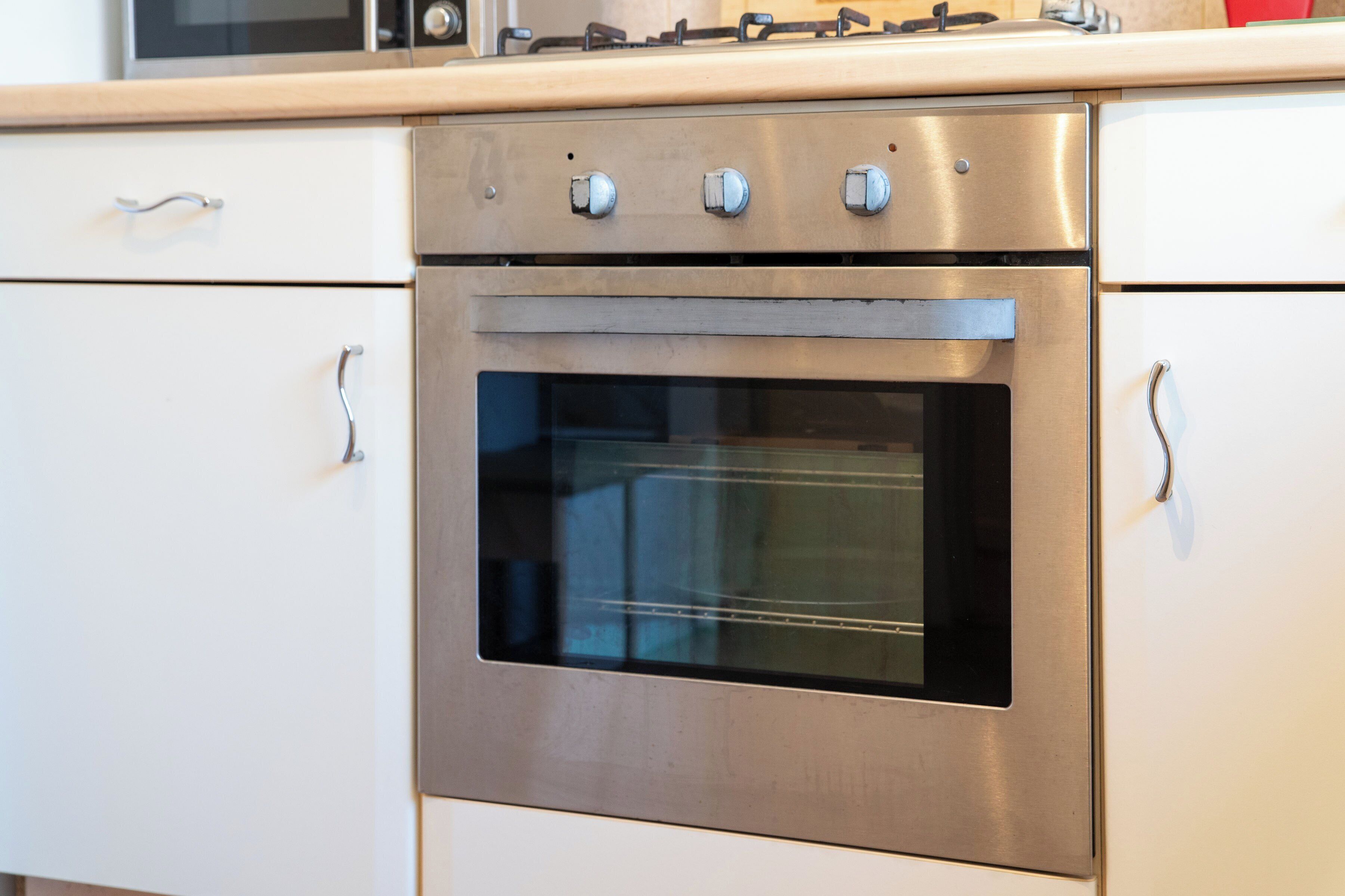 A stainless steel oven with four knobs, a glass window, and a white countertop above.