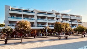 Un edifici de diverses plantes amb balcons, una zona per a vianants amb arbres i botigues.