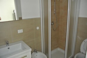 Casa de banho com chuveiro, lavatório, sanita e espelho.