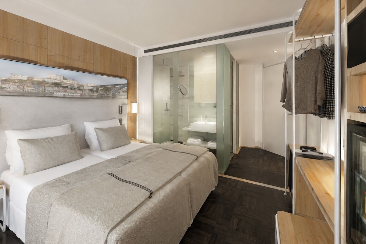 Une chambre d’hôtel moderne dotée d’un grand lit, d’une douche à parois de verre et offrant une vue sur le paysage urbain.