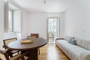 Ein modernes Wohnzimmer mit einem runden Holzesstisch, einer Couch und Blick durch eine offene Tür ins Freie.