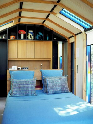 Ein Schlafzimmer mit Holzbalkendecke, einem Bett mit blauer Bettwäsche und einem Regal mit verschiedenen Gegenständen.