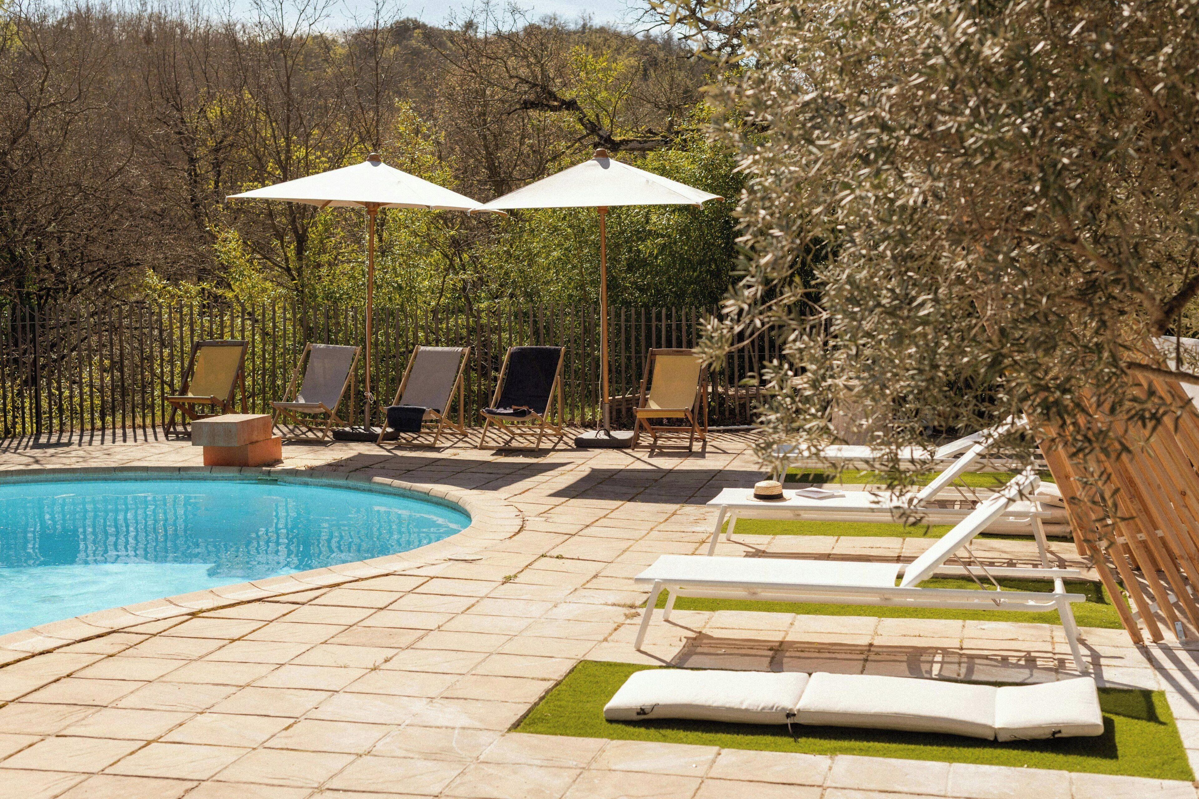 Un espace piscine aménagé avec des chaises longues, des parasols et un jardin clos.