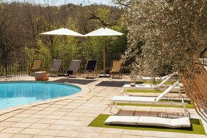 Ein Poolbereich mit Liegestühlen, Sonnenschirmen und einem eingezäunten Garten.