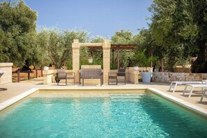 Ein Pool mit klarem Wasser, umgeben von Liegestühlen und einer Pergola mit hängenden Pflanzen.