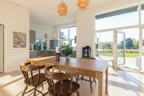 Un'ampia cucina con una grande isola, sedie in legno, lampade a sospensione e ampie finestre che offrono vista sul giardino.