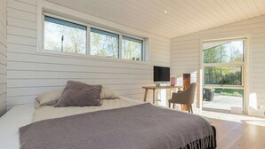 Quarto com cama, escrivaninha com computador e janela com vista para árvores.