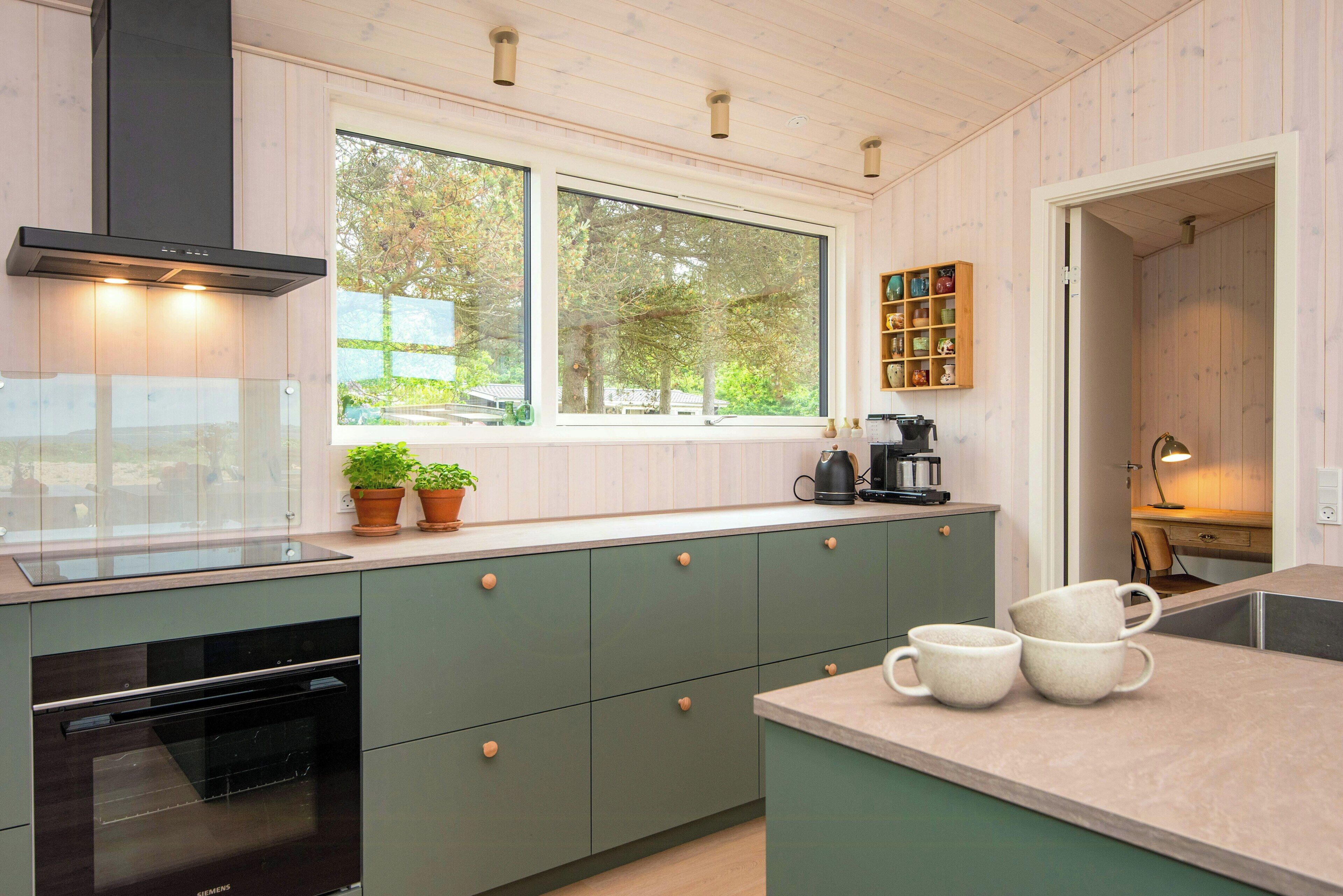A modern kitchen with a built-in oven, a window with a view of trees, and a coffee maker on the counter.