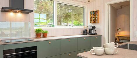A modern kitchen with a built-in oven, a window with a view of trees, and a coffee maker on the counter.