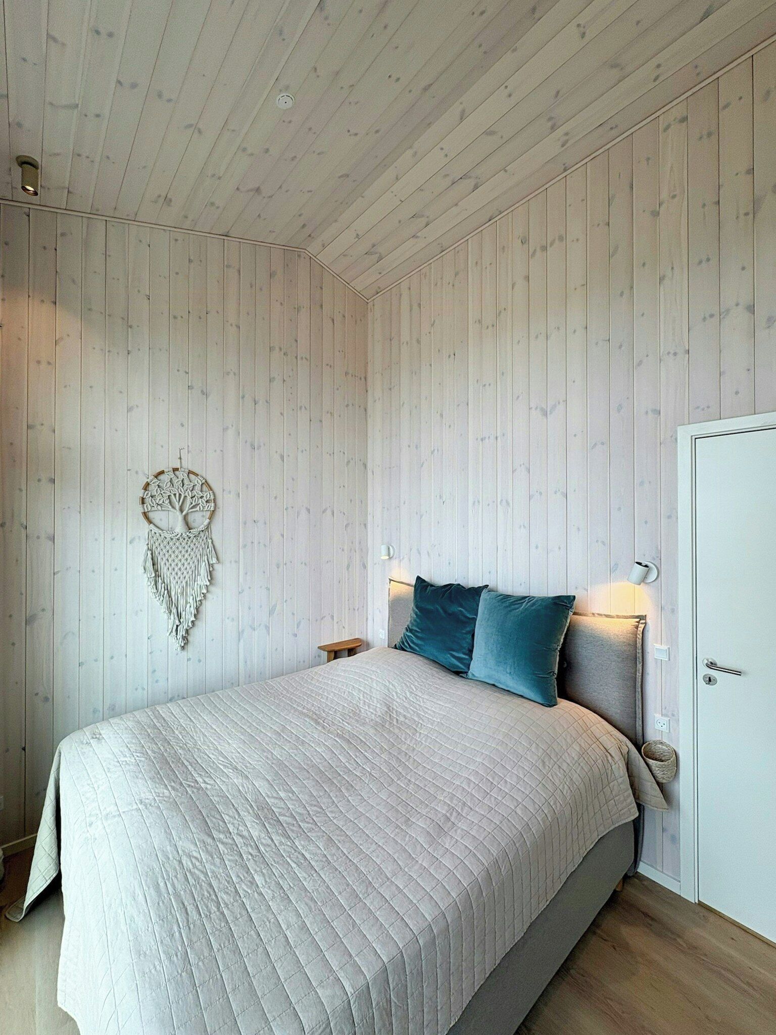 A bedroom with a bed, a wall-mounted macrame piece, and a door.