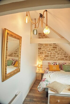 Ein Schlafzimmer mit schrägverdeckter Decke, einem großen Spiegel, einem Bett mit floralem Bettzeug und einer Steinwand.