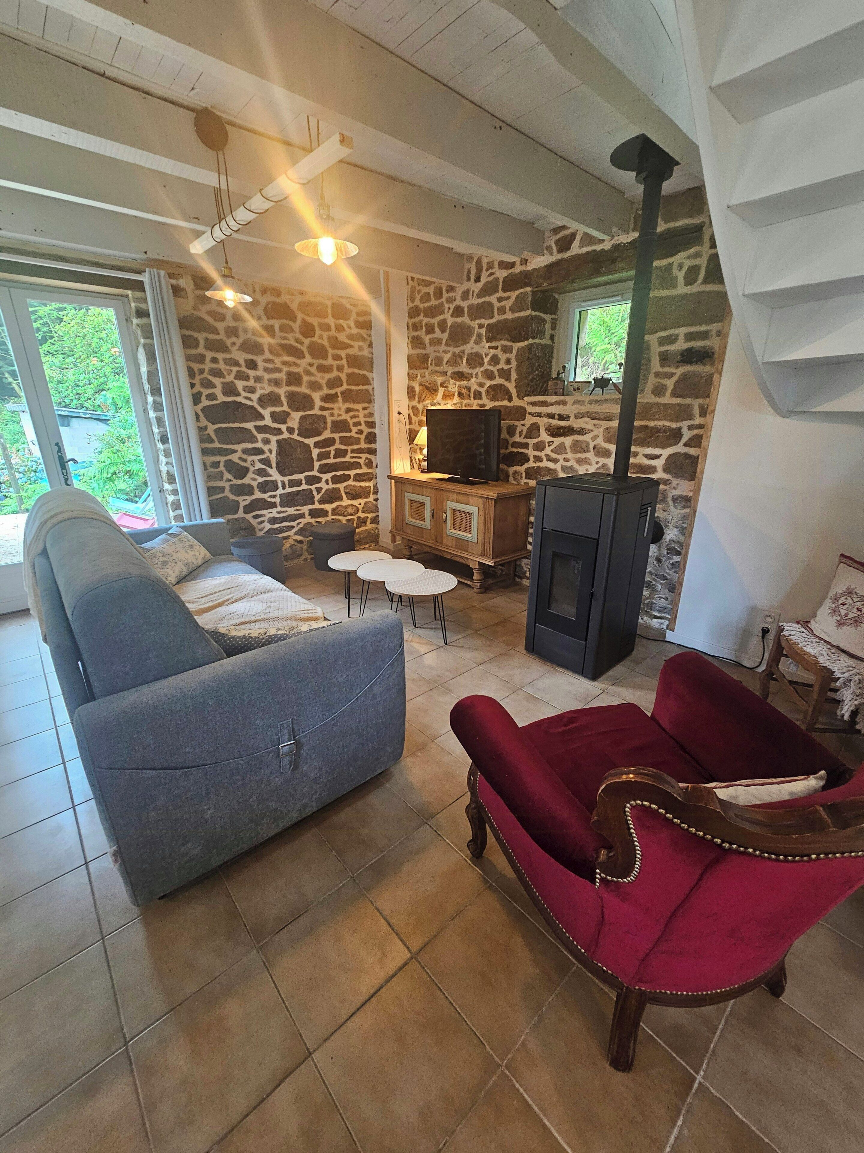 A living room with a stone wall, a fireplace, a sofa, a red armchair, and a television.
