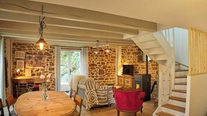 A cozy interior with a stone wall, a wooden dining table, a red chair, and a staircase. - Cottage in wooded heart of Brittany (Ploërdut)