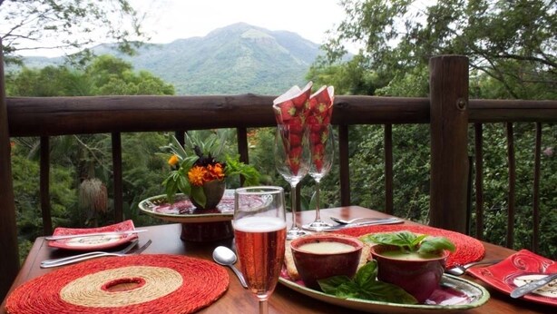 A table set with a glass of beverage, plates, cutlery, and a vase of flowers. - Old Joe's Kaia (Mbombela)